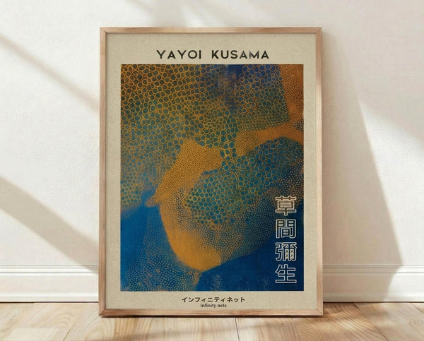 May include: Framed art print leaning against white wall on light wooden floor. The poster features abstract organic shapes in blue, orange and green with dotted texture patterns reminiscent of cellular structures. Text reads "Yayoi Kusama" at top and Japanese characters vertically on right side, with "infinity nets" at bottom. Natural wood frame with cream matting, soft natural lighting creates gentle shadows on wall.