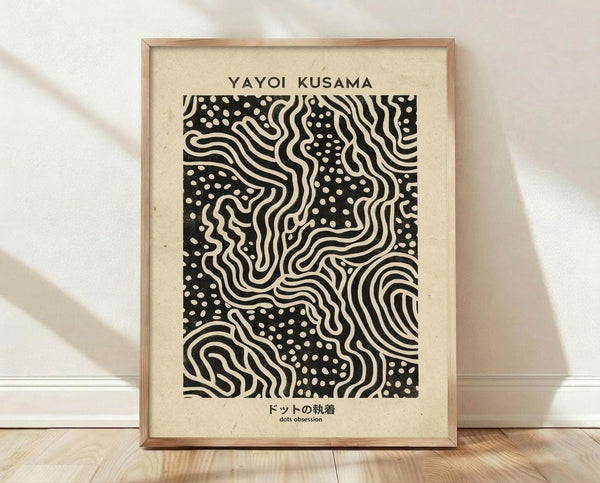 May include: Framed art print with cream background featuring black and white abstract pattern of flowing wavy lines and polka dots. Text reads "YAYOI KUSAMA" at top and Japanese characters with "dots obsession" below the artwork. Natural wood frame sits on light wooden floor against white wall with soft shadows.