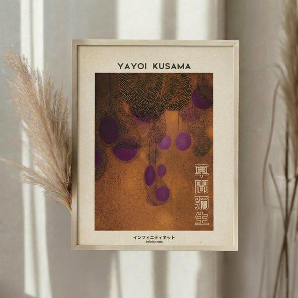 May include: Framed art print hanging on white wall featuring abstract pattern with orange and brown textured background, purple circular dots scattered across surface, and Japanese characters on right side. Dried pampas grass visible in left corner. Cream-colored wooden frame with white matting surrounds artwork in minimalist interior setting.