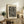 May include: Black and white abstract art print with flowing wavy lines and polka dots in wooden frame, displayed on rustic wood sideboard next to small fern plant, brown leather chair, ceramic vases and books in neutral-toned living room setting