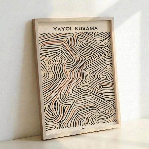 May include: Framed art print with flowing abstract wave patterns in black, brown and cream tones against cream background. Text "YAYOI KUSAMA" appears at top. Light wood frame leans against white wall, showing organic curved lines that create mesmerizing swirling motifs reminiscent of topographical maps or flowing water.