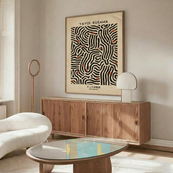 May include: Framed poster with black and white wavy line pattern and red accents displayed above wooden sideboard in modern living room. White curved chair and oval glass coffee table with colorful abstract art visible. Minimalist interior with neutral walls and natural lighting.