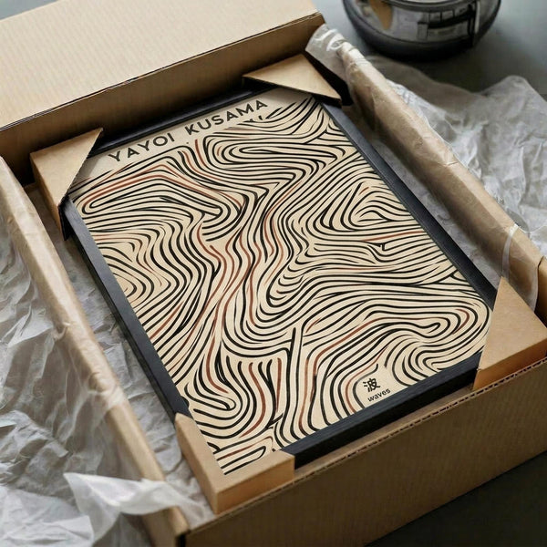 May include: Framed art print with flowing, swirling wave-like lines in black, brown, and cream tones, displayed in a cardboard shipping box with protective wrapping. The abstract topographical pattern creates organic, undulating forms across the surface. Wooden dowels and tissue paper are visible as packaging materials around the black-framed piece.