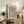 May include: Framed art print with flowing wavy lines in brown and black tones on cream background, displayed on rustic wooden sideboard alongside decorative pottery, books, and fern plant in neutral-toned living room setting with beige upholstered furniture.
