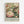 May include: Framed poster print featuring a detailed hummingbird with iridescent green and teal feathers hovering among large pink and cream peonies with lush green foliage. The vintage-style artwork has soft, muted colors on a sage green background. White text at bottom reads "CENTENARY EXHIBITION WILLIAM MORRIS" with exhibition details. Light wood frame hangs against white wall.