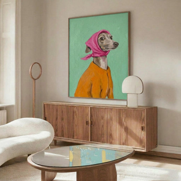 May include: Portrait painting of an Italian Greyhound wearing a pink headscarf and orange jacket against mint green background, displayed in thin wooden frame above walnut credenza in modern living room with cream chair, glass coffee table, and white table lamp