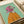 May include: Framed artwork showing an Italian greyhound wearing a pink headscarf and orange sweater against a mint green background, displayed on a white surface next to rolled white paper and cream ribbon