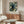 May include: Framed vintage-style poster featuring a black cat among blue and cream floral William Morris-inspired textile pattern, displayed above a walnut wood credenza in a modern living room with white curved chair, glass coffee table, and floor lamp
