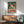 May include: Vintage-style poster featuring a whimsical frog character with large orange eyes and red markings, displaying "TOKYO" in bold red letters with Japanese characters above on a teal background. Framed artwork hangs above a wooden mid-century modern credenza with table lamp, positioned next to a sage green upholstered armchair with wooden frame in a bright, minimalist living room setting.