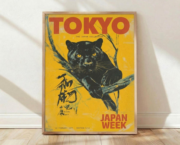 May include: Framed vintage-style poster with yellow background featuring a black panther with golden eyes perched on a tree branch. Bold red text reads "TOKYO" at top and "JAPAN WEEK" at bottom, with Japanese characters on left side. Date shows "12 FEBRUARY 1977 - EDITION 5/12". Light wooden frame displayed on wooden floor against white wall with natural lighting and shadows.