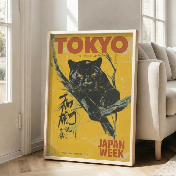 May include: Vintage-style poster with yellow background featuring black panther on tree branch, red "TOKYO" text at top and "JAPAN WEEK" at bottom, Japanese characters on left side, displayed in white frame leaning against white wall next to beige sofa in bright living room with hardwood floors and large windows.