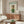 May include: Fashion magazine-style poster featuring a white poodle wearing green knit sweater, wicker head covering, and round sunglasses against cream background with "DOGUE" text in teal letters. Wooden-framed print displayed above mid-century walnut credenza with brass hardware in modern living room setting with white upholstered chair, glass oval coffee table, and minimalist table lamps.