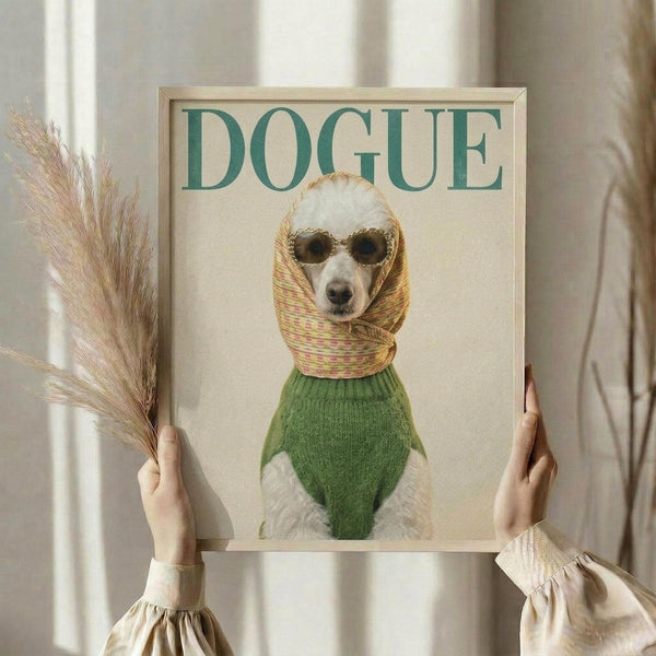 May include: Framed poster showing a small white dog wearing sunglasses, yellow patterned headscarf, and green sweater styled like a fashion magazine cover with "DOGUE" text at top. Person in cream ruffled sleeves holds the light wood frame against white curtained window, with dried wheat stems visible on left side.