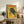 May include: Framed vintage-style yellow poster featuring a black panther on tree branches with Japanese text and "TOKYO" and "JAPAN WEEK" in red lettering, displayed on rustic wooden sideboard alongside fern plant, ceramic vase, stacked books, and beige armchair in neutral-toned living room setting