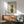 May include: Framed poster featuring white poodle wearing dark sunglasses, green knit sweater and colorful patterned headscarf with "DOGUE" text at top in green letters. Displayed in modern living room with light wood credenza, white ceramic table lamp, mint green upholstered armchair with wooden frame, and round coffee table. Natural sunlight creates geometric shadows on white wall.