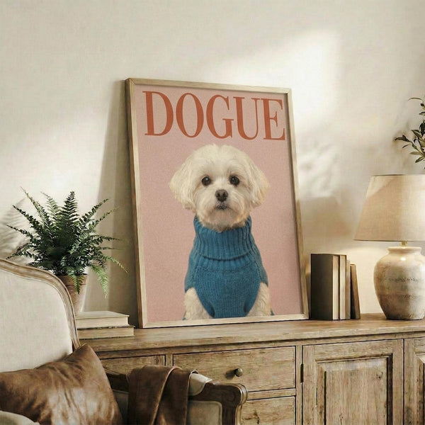 May include: Framed poster showing a small white fluffy dog wearing a blue turtleneck sweater against a pink background with "DOGUE" text in red letters, displayed on a rustic wooden sideboard alongside books, a ceramic vase, and fern plant in a cozy living room setting with warm lighting