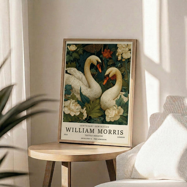 May include: Framed botanical poster featuring two white swans with orange beaks surrounded by cream peonies and green foliage on dark background, displayed on round wooden side table next to beige upholstered chair in sunlit room with white curtains and plant shadows