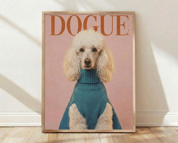 May include: Framed poster print leaning against white wall on light wood floor with soft natural lighting. Features a white poodle with curly groomed fur wearing a teal blue turtleneck sweater against a dusty pink background. Orange text reading "DOGUE" appears at top in magazine-style lettering. Thin natural wood frame surrounds the artwork.