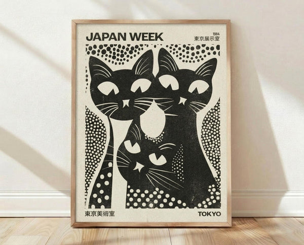 May include: Framed vintage-style poster featuring three stylized black cats with white accents in bold graphic design. Poster shows halftone dot patterns, "JAPAN WEEK" and "1984 TOKYO" text with Japanese characters. Light wood frame displayed against white wall on wooden floor with natural lighting and shadows.