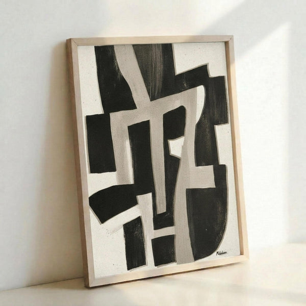 May include: Abstract black and white geometric artwork in light wood frame leaning against white wall. Bold angular shapes and curved forms create dynamic composition with contrasting dark and light areas. Canvas shows textured brushwork with organic flowing elements intersecting geometric forms.