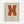 Orange letter X painted in brushstroke style on cream textured background, displayed in light wood frame on white wall. Below the X is black text reading "ELLSWORTH KELLY FROM TUESDAY, MARCH 15, 1966 FERUS GALLERY LOS ANGELES, CALIFORNIA". The artwork has a minimalist, mid-century modern aesthetic with visible paint texture and slightly rough edges on the letterform.