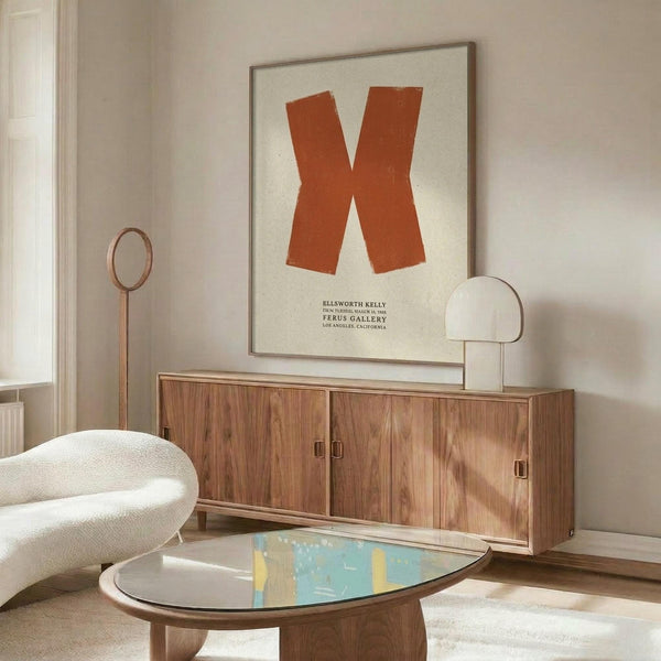 May include: Orange letter X poster on cream background displayed above mid-century walnut credenza in minimalist living room with white sculptural chair, glass coffee table, and modern brass floor lamp. Warm natural lighting creates soft shadows across neutral walls.