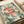 Japanese-inspired artwork featuring three red fish with spotted patterns and large dark eyes swimming among teal green seaweed and coral-colored sea anemones. The illustration uses a muted color palette of coral pink, sage green, and cream with decorative dots and organic flowing elements. The print is displayed on cream paper with rolled paper visible in the background, showing fine textural details and botanical motifs throughout the underwater scene.
