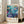 May include: Framed underwater scene poster with colorful fish, coral, and sea life in blues, purples, and oranges, featuring Japanese text and "JAPAN 1984" with museum attribution. Light wood frame leaning against white wall next to beige sofa in bright, minimalist room with large windows.