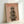 May include: Framed poster print leaning against white wall showing a whippet or greyhound wearing a herringbone flat cap and furry brown coat against a pink background, with "DOGUE" text in orange letters at top, displayed in light wooden frame on white surface