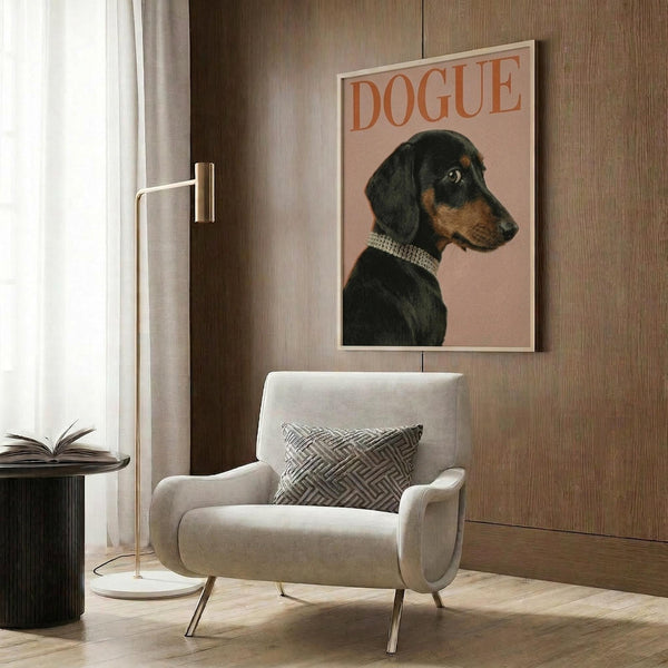 May include: Framed poster showing a black and tan dachshund wearing a pearl collar against a pink background with "DOGUE" text in orange letters, displayed on wood paneled wall above cream upholstered chair with geometric patterned pillow, brass floor lamp and side table with open book nearby