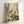 May include: Framed botanical art print leaning against white wall, featuring stylized wildflowers and plants in dotted pattern style reminiscent of pointillism. Artwork shows purple feathery grasses, white daisy-like flowers with yellow centers, golden seed heads, and burgundy blooms against cream background. Natural wood frame complements the earthy color palette of greens, purples, yellows, and browns throughout the meadow scene.