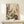 May include: A framed botanical art print featuring stylized wildflowers and plants in dotted textures, displayed on a light wood console table against a cream wall. The artwork shows purple lupines, white daisies with yellow centers, golden seed heads, and burgundy blooms in an abstract meadow style. A small white gift box with twine sits beside the wooden-framed print.