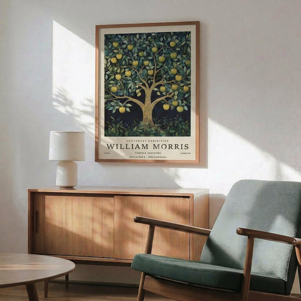 May include: Framed William Morris exhibition poster featuring apple tree with golden fruit and dark green foliage, displayed above walnut credenza with ceramic lamp in mid-century modern living room with sage green armchair and natural lighting casting shadows on white wall.