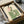 May include: Framed art print in black frame showing woman in green striped dress with floral pink top, sitting gracefully. Illustration has vintage-inspired style with cream background. Frame appears in cardboard shipping box with protective tissue paper wrapping. Wooden rolling pin visible beside packaging materials on white surface.