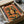 May include: Vintage-style poster with orange and green color scheme featuring stylized woman's face surrounded by citrus fruits and leaves, displayed in black frame inside cardboard shipping box with protective wrapping materials on white surface