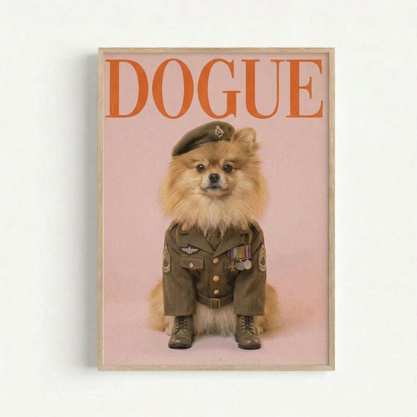 A framed poster featuring a fluffy Pomeranian dog dressed in an olive green military uniform with medals, brass buttons, and a matching beret. The dog wears black combat boots and stands against a soft pink background. The word "DOGUE" appears in large orange letters at the top, styled like a fashion magazine cover. The artwork is displayed in a light wooden frame against a white wall.