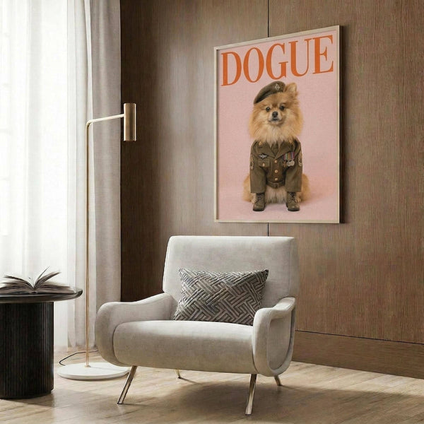 May include: Framed poster on wood-paneled wall showing a fluffy Pomeranian dog wearing olive green military uniform with beret and boots against pink background, with "DOGUE" text in orange letters at top. Modern beige armchair with patterned pillow, gold floor lamp, and dark side table with open book complete the contemporary room setting.