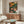 May include: Colorful botanical poster with stylized flowers and leaves in orange, pink, yellow, and green tones displayed above a mid-century modern wooden credenza. Room features white curved chair, oval glass coffee table, floor lamp, and neutral walls with natural lighting.