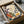 May include: Framed botanical art print in dark frame, nestled in cardboard shipping box with brown paper wrapping. The artwork features stylized flowers and plants in warm autumn colors - burgundy, orange, yellow, and teal - with decorative patterns including dotted circles and delicate stems. White tissue paper and kraft paper packaging materials surround the frame inside the box.