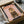 May include: Framed poster print in black frame being unpacked from cardboard box with tissue paper. Shows Pomeranian dog wearing olive green military uniform with medals and beret on pink background. Large orange "DOGUE" text at top. Frame sits among white packing materials on neutral surface.