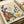 May include: Vintage-style botanical poster print displayed on white bedding featuring stylized flowers in purple, orange, yellow, and teal colors with decorative patterns and leaves. The cream-colored print shows "OSAKA '82" and "FLOWER MARKET" text at bottom, surrounded by natural lighting and soft textile textures.