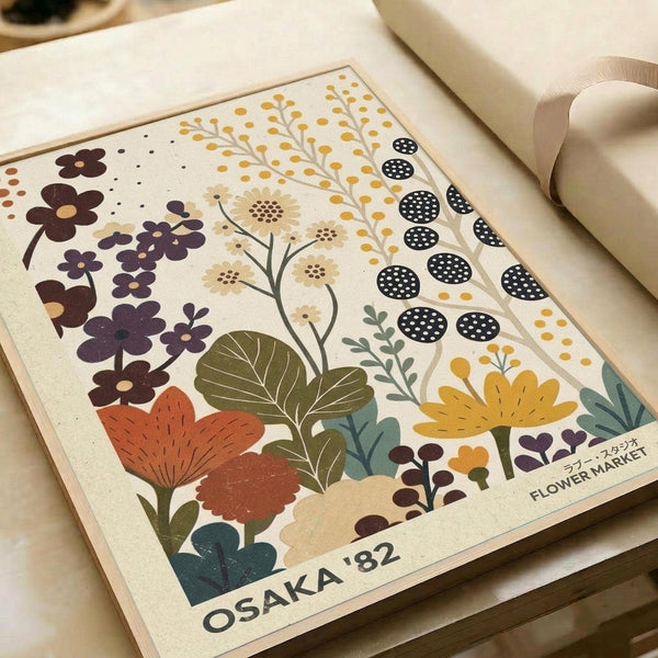 May include: Vintage-style botanical poster print displayed on white bedding featuring stylized flowers in purple, orange, yellow, and teal colors with decorative patterns and leaves. The cream-colored print shows "OSAKA '82" and "FLOWER MARKET" text at bottom, surrounded by natural lighting and soft textile textures.