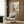 May include: Framed botanical wall art featuring stylized flowers and plants in autumn colors - purple, orange, yellow, and green - displayed above a beige upholstered chair with geometric throw pillow. Modern living room setting with wood paneled walls, brass floor lamp, and dark side table with open book.