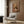 May include: Framed poster on wood-paneled wall featuring a golden cocker spaniel wearing a tan suit jacket with flower boutonniere on magazine-style cover reading "DOGUE." Modern living room setting with cream armchair, geometric throw pillow, gold floor lamp, and dark side table with open book.