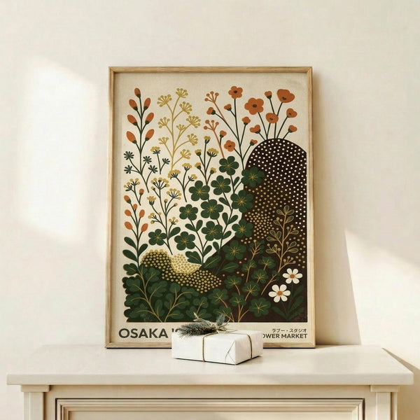 May include: Framed botanical poster with stylized wildflowers and plants in warm earth tones - oranges, greens, and browns - featuring dotted abstract shapes and delicate stems against cream background. Natural wood frame sits on light wooden shelf beside small white wrapped gift with evergreen sprig. Minimalist white wall backdrop creates clean, modern styling.
