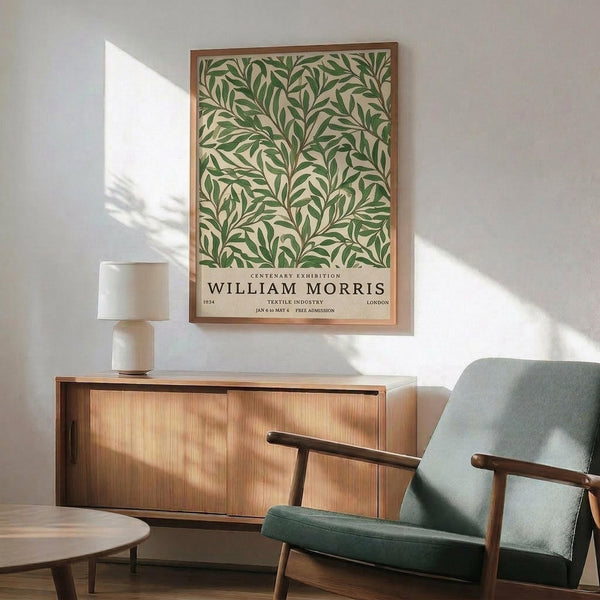 May include: Vintage-style botanical poster featuring green leafy pattern on cream background with "William Morris" text, displayed in thin wooden frame above mid-century modern wooden sideboard. Scene shows sage green upholstered armchair with wooden arms, small round coffee table, and white ceramic table lamp. Warm natural sunlight creates geometric shadows on white wall, giving the room a serene, minimalist aesthetic with earthy tones throughout.