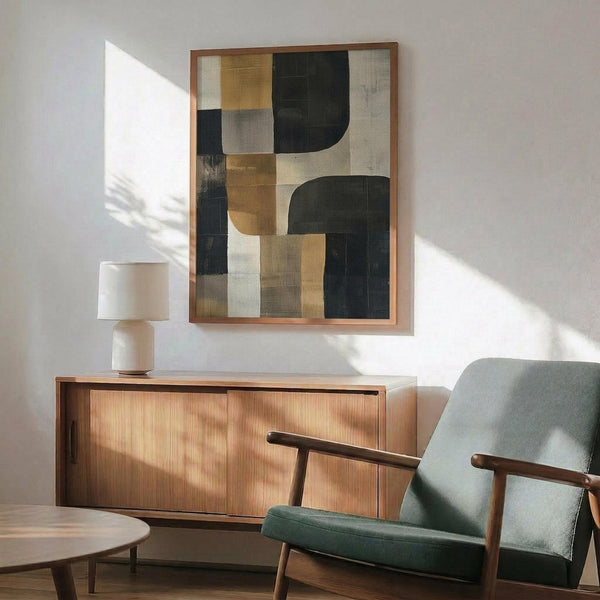 May include: Abstract geometric artwork with black, golden yellow, gray and cream colored shapes in wooden frame, displayed above mid-century modern walnut credenza with ceramic table lamp, next to sage green upholstered armchair with wooden arms in sunlit minimalist living room
