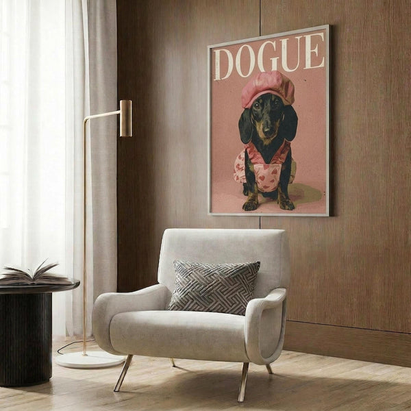May include: Framed poster featuring a black and tan dachshund wearing a pink chef's hat and floral apron on coral pink background with "DOGUE" text at top, displayed above a cream upholstered armchair with geometric pillow in modern living room with wood paneled walls, brass floor lamp, and side table with open book.