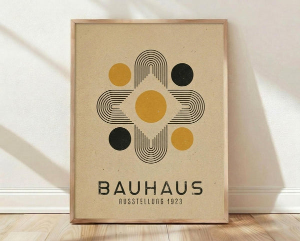 May include: Framed Bauhaus-style poster with geometric design featuring concentric rounded rectangles in black lines surrounding yellow and dark green circles on beige textured background, displayed against white wall on light wooden floor with natural lighting casting soft shadows