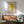 May include: Mid-century modern living room with framed yellow abstract star-shaped artwork on white wall above wooden credenza. Green upholstered armchair with wooden frame, small round coffee table, and ceramic table lamp visible. Warm natural lighting creates geometric shadows across the minimalist interior space.